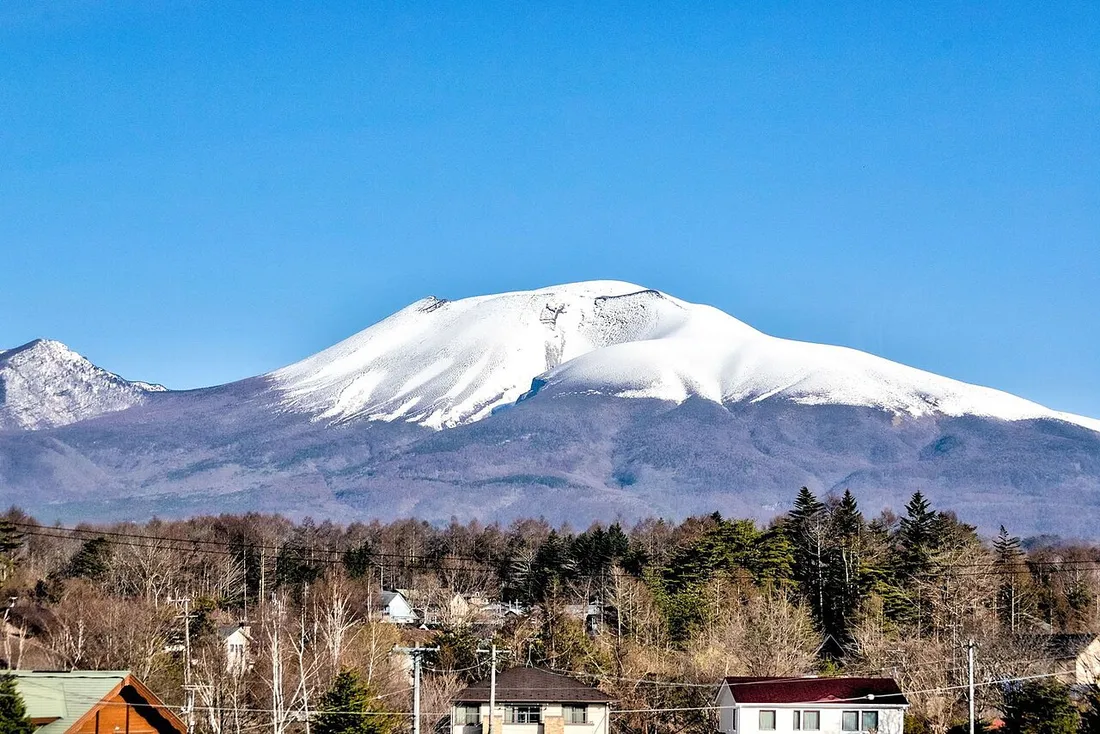 青空の下、雪をかぶった浅間山と、手前の森や住宅地