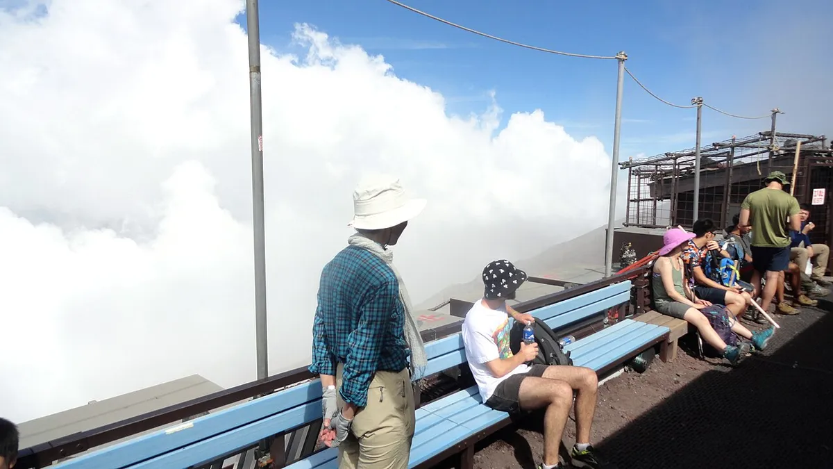 山小屋の外のベンチで休む登山者と雲海