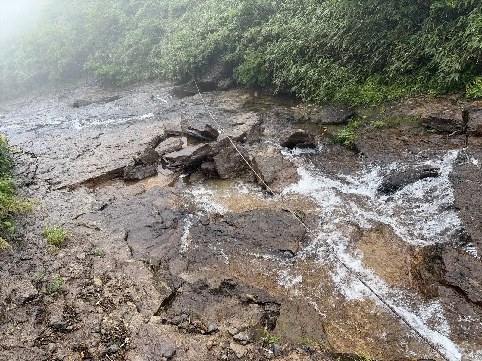 岩の間を白く泡立って流れる沢と、沢を横切るように張られたロープ