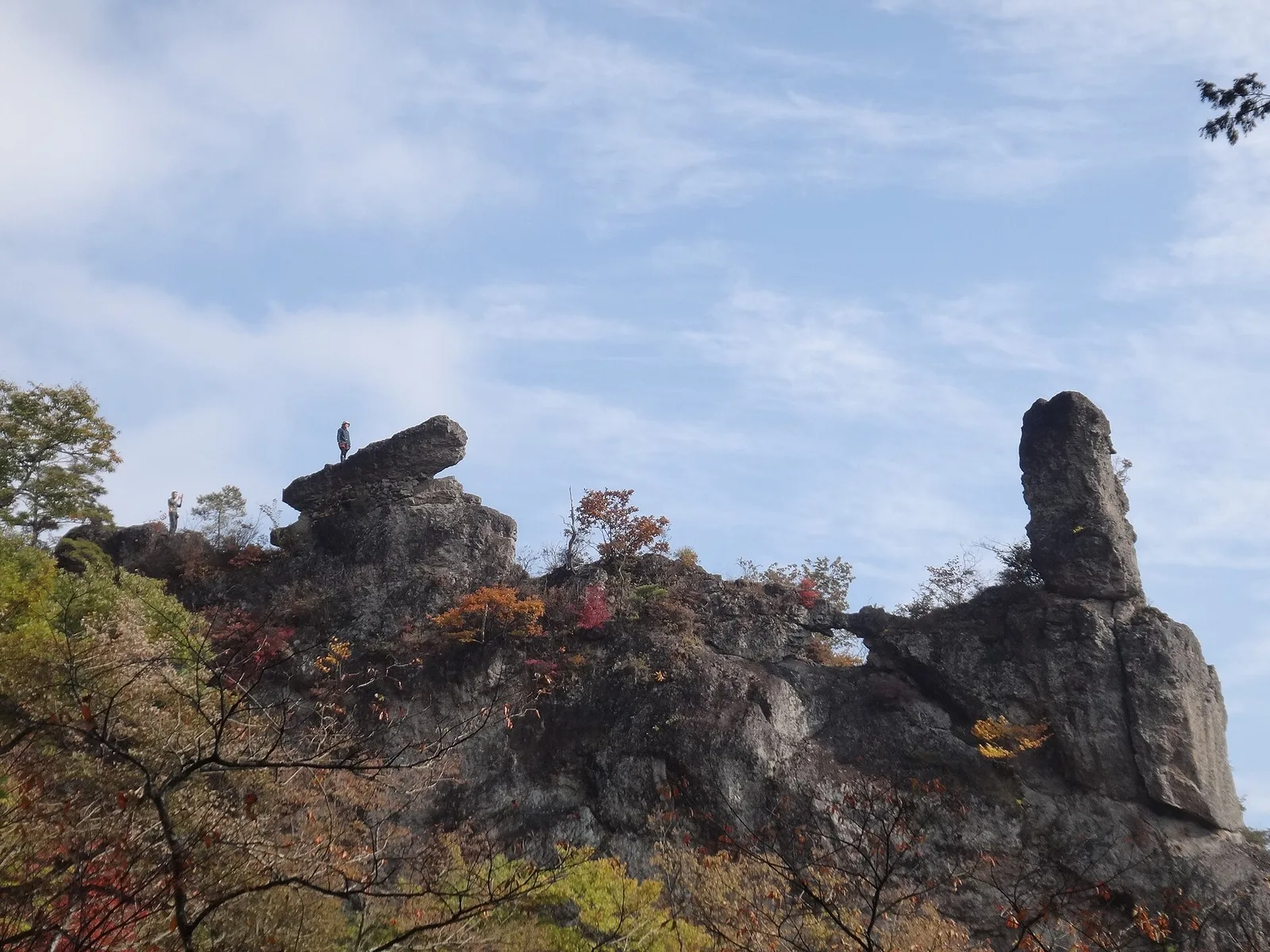 紅葉した木々の上に突き出す大砲のような形の岩と、その右に立つ細長い岩峰