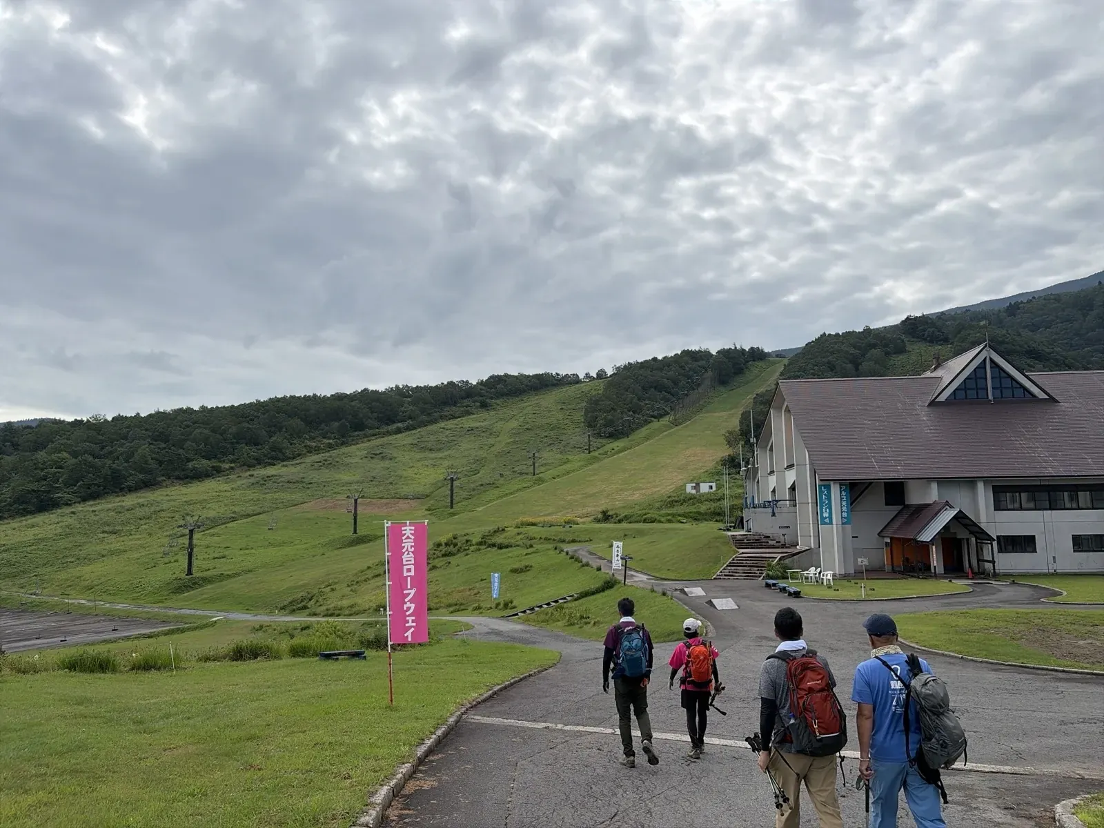 天元台高原駅の近く。「天元台ロープウェイ」ののぼりと、ゲレンデの斜面に並ぶリフトの支柱、建物へ続く舗装された道