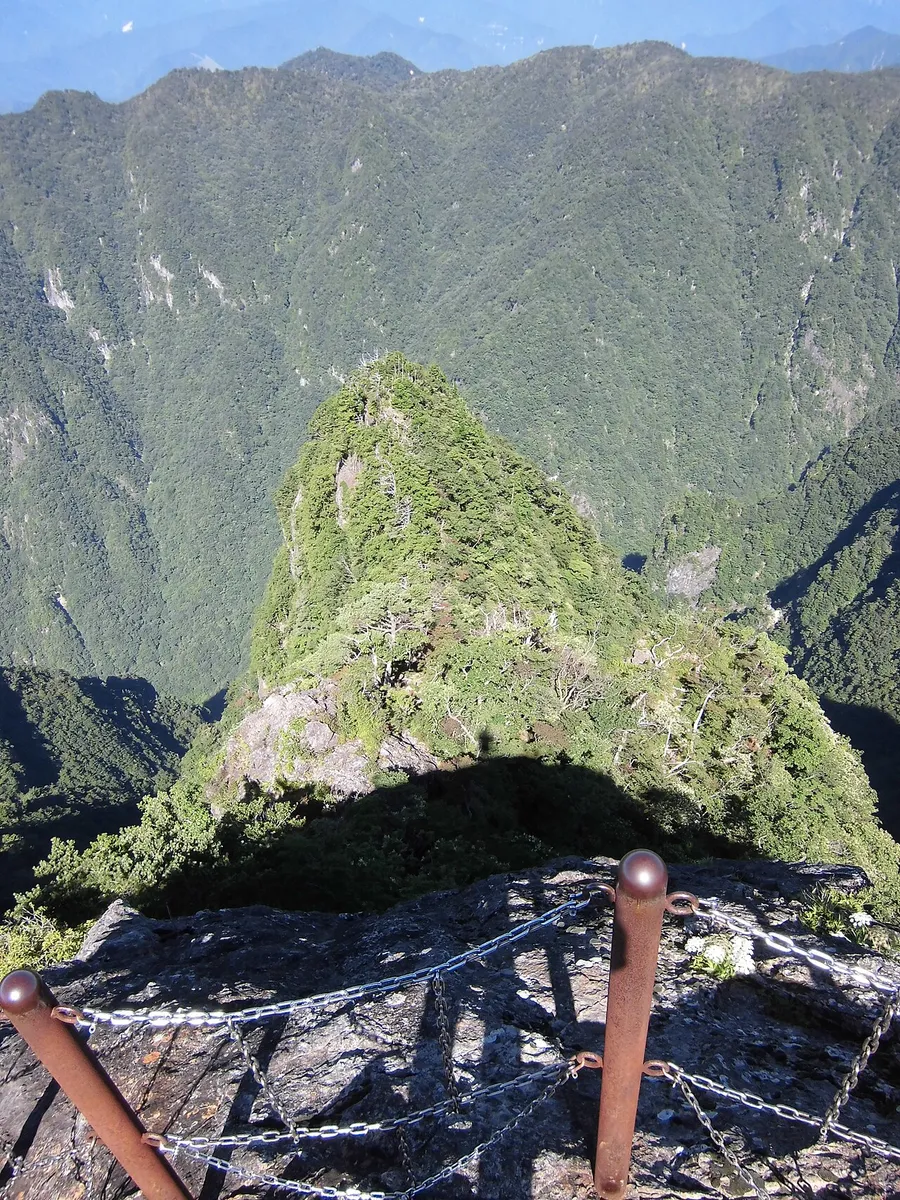 大蛇嵓の断崖の先端に立つ岩と、谷を挟んだ緑の山