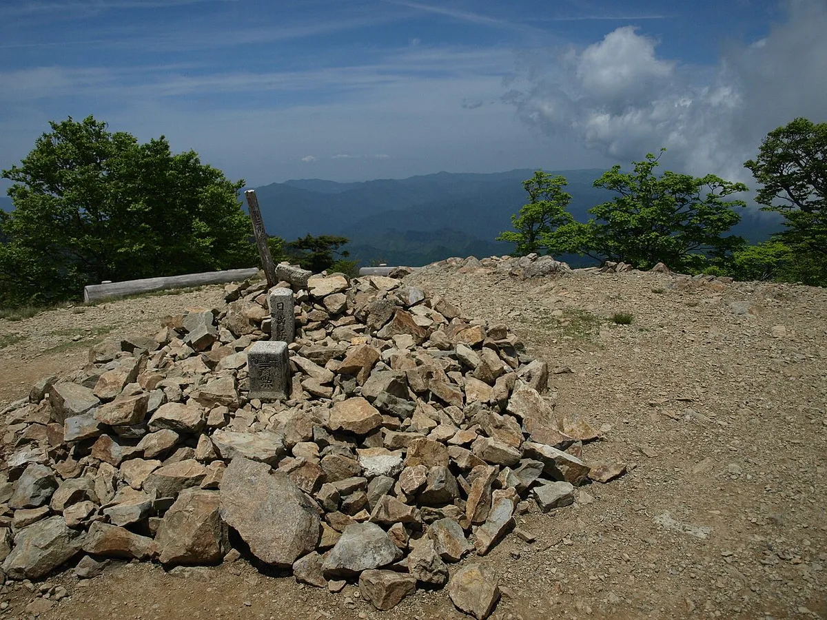 日出ヶ岳の山頂に積まれた石と背景の山並み