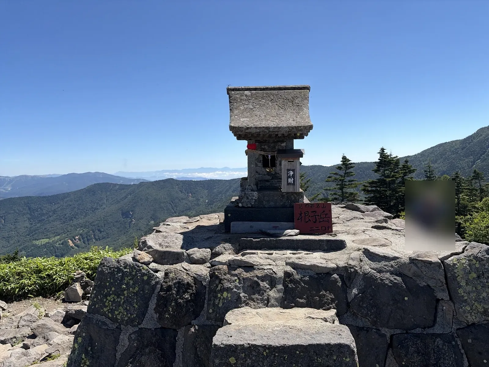 根子岳の山頂。石積みの台の上の祠と、「花の百名山 根子岳 二二〇七」の看板