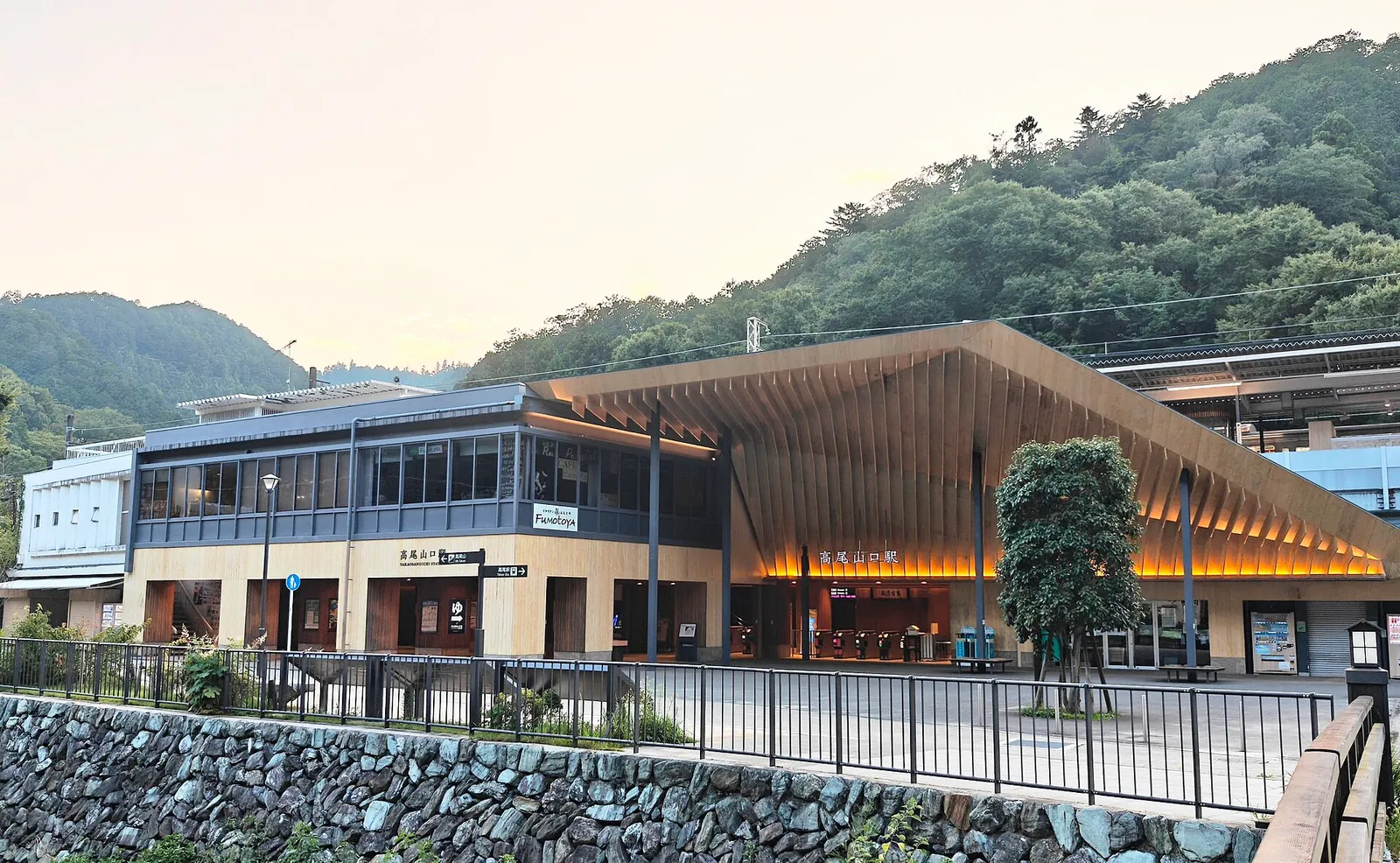 木の大屋根が特徴的な京王線高尾山口駅の駅舎と、背後の緑の山