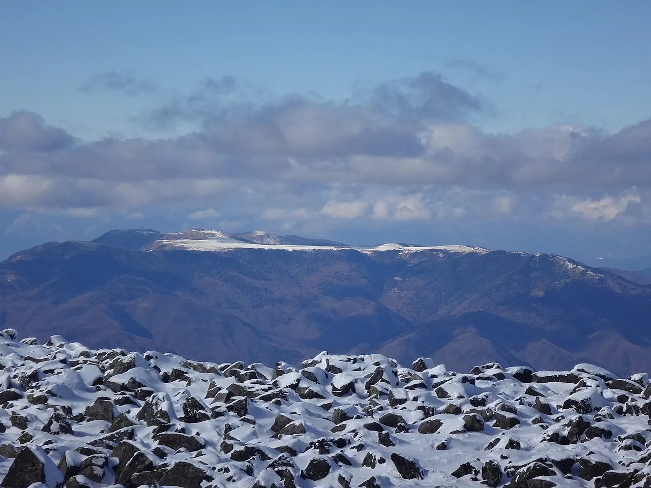 蓼科山山頂から北西方向に望む美ヶ原の台地と、その奥に連なる北アルプスの山並み